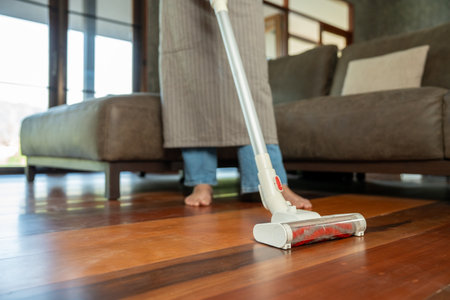 Housewife using vacuum cleaner on the floor. Wearing an apron to clean the living room at house. Young woman is happy to clean home. Maid cleaning service.の写真素材