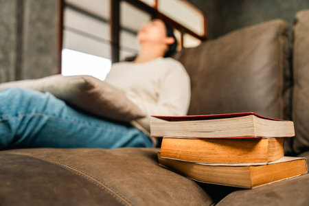Sleeping Asian beautiful woman lay down on cozey couch sofa while reading book in living room with warm light at night. People female reading book until fall asleep stay home part time relax at homeの写真素材