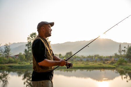 Excited emotion of Handsome fisherman fishing as a leisure activity during his vacation at the lake on sunset. Relax and hobby concept.の写真素材