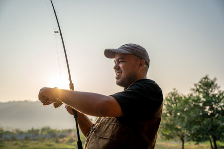 Excited emotion of Handsome fisherman fishing as a leisure activity during his vacation at the lake on sunset. Relax and hobby concept.の写真素材