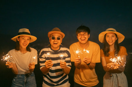Happy friends cheering with fireworks at beach party outdoor. People vacation holiday on beach. Summer holiday having fun relax vacation time in the eveningの写真素材