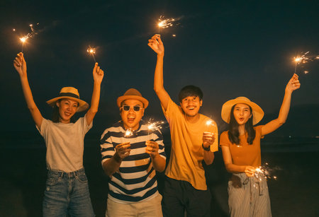 Happy friends cheering with fireworks at beach party outdoor. People vacation holiday on beach....