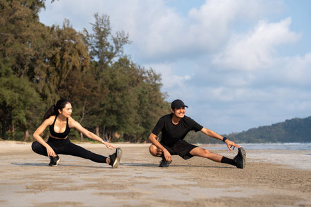 Asian Couple stretching arms and legs before running outdoors sea sand beach. Sporty people warm up body before jogging. Athlete running during sunset on the beach. Workout exercise.の写真素材