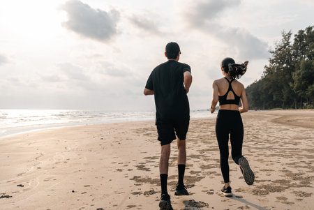 Asian Couple jogging and running outdoors sea sand beach. Sporty people wearing sportswear jogging. Male female athlete running during sunset on the beach. Workout exercise. Healthy and lifestyle.の写真素材