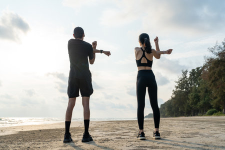 Asian Couple stretching arms and legs before running outdoors sea sand beach. Sporty people warm up body before jogging. Athlete running during sunset on the beach. Workout exercise.の写真素材
