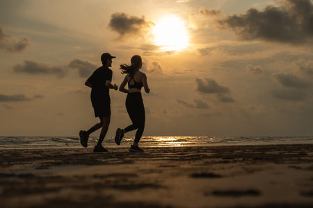 Asian Couple jogging and running outdoors sea sand beach. Sporty people wearing sportswear jogging. Male female athlete running during sunset on the beach. Workout exercise. Healthy and lifestyle.の写真素材