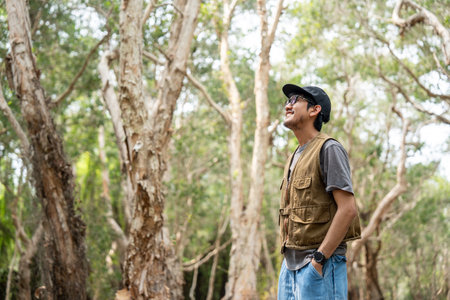 Young asian man traveling alone in the forest. Happy weekend on vacation time. Attractive male traveler walking in nature spend time enjoy with holidayの写真素材