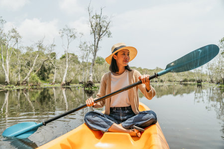 Holiday travel activities. Happy asian woman rowing a canoe or kayak in mangrove forests. Young traveler with kayak at botanical garden tropical mangrove forest in a national park.の写真素材
