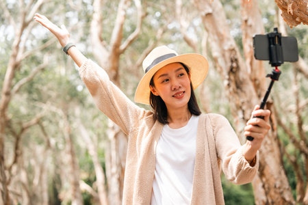 Young asian female travel vlogger with smartphone alone in the forest. Happy weekend on vacation time. Attractive woman traveler in nature  enjoy with holiday recording video sharing on social mediaの写真素材