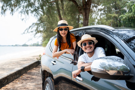 Young asian couple man and woman travel by car on a bright day to the sea sand beach with beautiful blue sky sunlight. They was happy along the way trip. safety driving car vacation.の写真素材