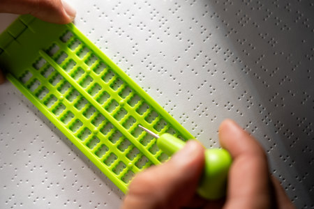 Close up Hand of a blind person writing some braille text on page paper. Young blind man using slate and stylus tools making embossed printing the braille alphabet Code on sheet.の写真素材