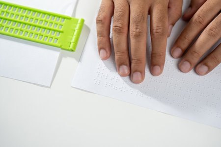 Hand of a blind person reading some braille text on page paper to learn. Finger of blind student...