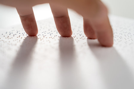 Hand of a blind person reading some braille text on page paper to learn. Finger of blind student...