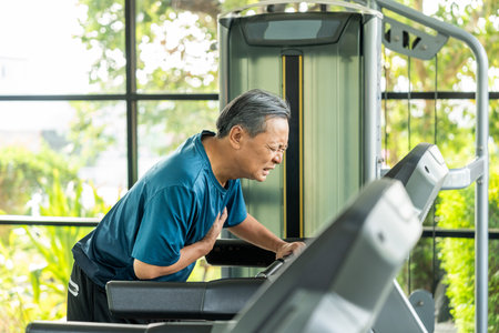 Senior sporty person in sports uniform running on treadmill. Old man  he felt a pain in his chest held his hand and squeezed it. Mature Heart attack that needed treatment.の写真素材