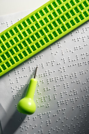 Close up Hand of a blind person writing some braille text on page paper. Young blind man using slate and stylus tools making embossed printing the braille alphabet Code on sheet.の写真素材
