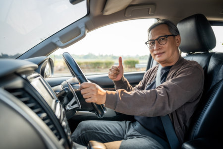 Senior Asian man drives a car vehicle on a clear day. With beautiful blue sky. He smiling driving to travel by car. Old man getting new car.の写真素材