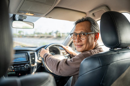 Senior Asian man drives a car vehicle on a clear day. With beautiful blue sky. He smiling driving to travel by car. Old man getting new car.の写真素材