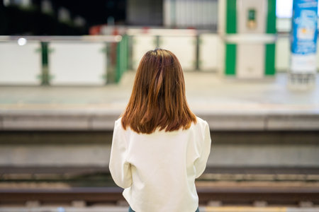 Rear view asian woman using smartphone application navigate location destination while travel by train. Asian female with cell phone standing near railway platform in train station.の写真素材