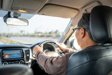 Senior Asian man drives a car vehicle on a clear day. With beautiful blue sky. He smiling driving to travel by car. Old man getting new car.の写真素材