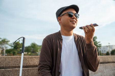 Young asian blind man using application on mobile phone to helping accessibility for persons with visual impairment. Technology for blind people sending voice message or navigation.