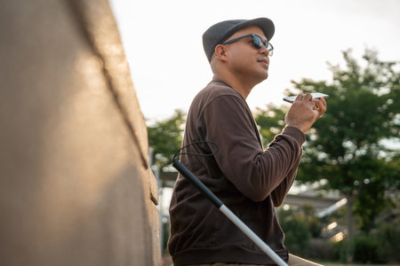 Young asian blind man using application on mobile phone to helping accessibility for persons with visual impairment. Technology for blind people sending voice message or navigation.の写真素材