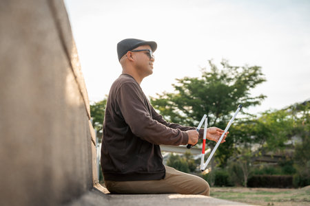 Young asian blind man sitting outside holding walking stick Visually impaired man difficult to...