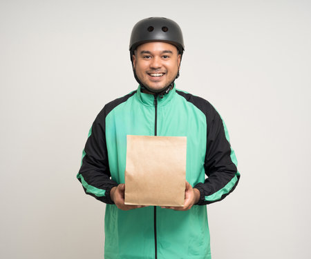 Young asian rider wearing green jacket uniform and bike helmet various action holding food paper bag delivery to customer. Male delivery service worker. Courier and shipping food service.の写真素材