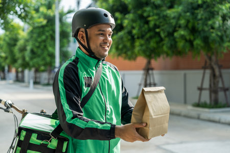 Portrait Rider food delivery man wearing green uniform and helmet cycling a bicycle the food service to customer. Happy delivery man with green backpack shipping of goods to customers.の写真素材