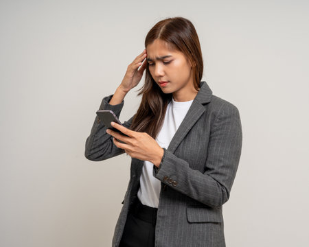 Pretty young asian woman using smartphone feeling upset confused bad depressed emotional standing on isolated white background. Holding cell phone. Thinking and stressedの写真素材