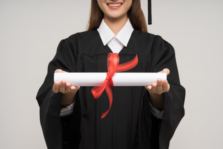 Happy asian woman in graduation costume with cap holding diploma on isolated background. College degree successful education graduation in universityの写真素材