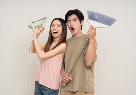 Housekeeper Happy asian couple attractive in various action gesture holding iron and broom on isolated white background. Cheerful Smiling young man and woman clean house togetherの写真素材