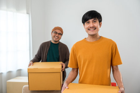 The couple asian family buying new house. Moving relocation with parcel box cardboard. They relax in living room lifestyle.の写真素材