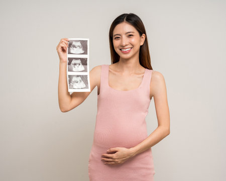 Happy Pregnant asian woman stroking touch belly motherhood with ultrasound photo on isolated background. Family planning maternity and pregnancy with insurance for child health.の写真素材
