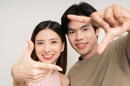 Happy asian couple attractive in various action gesture standing on isolated white background. Cheerful Smiling young man and woman showing frame size for taking photoの写真素材