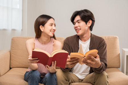 Happy moment of asian family man and woman husband and wife just married buying new house. Relax reading book on sofa in living roomの写真素材