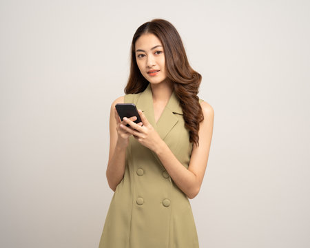 Young asian woman using cellphone standing on isolated white background. Happy Excited Beautiful young asian shopping online payment with mobile phone. Playing game on smartphoneの写真素材