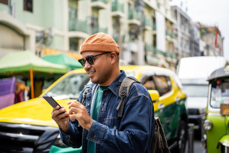 Asian traveling backpacker in Khao San Road outdoor market in Bangkok Thailand. Using mobile phone application to navigate the location. Tourist walking in the downtown street traditional marketの写真素材