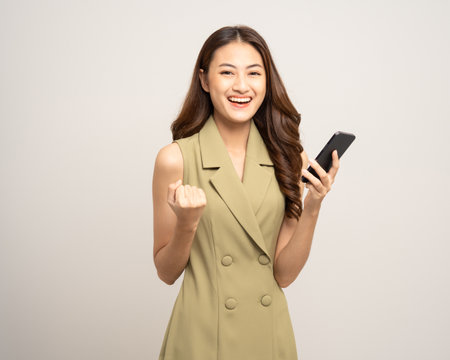 Pretty young asian woman using cellphone standing on isolated white background. Happy Excited Beautiful young asian shopping online payment with mobile phone. Playing game on smartphoneの写真素材