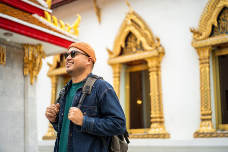 Young Asian traveling backpacker walking in temple at Bangkok Thailand. Happy tourist walking in the downtown street traditional ancient temple. Holiday vacation time touristの写真素材