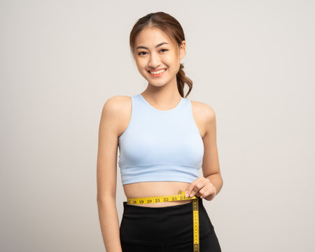 Young woman measuring her waistline with measure tape. Weight loss diet session. Woman in sportswear slim fit and firm body shape. Care about eating and workout exercise.の写真素材