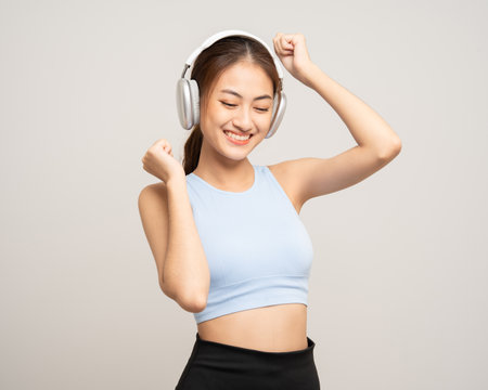 Young beautiful asian woman with sportswear listen to music by headphone on isolated white background. Attractive Portrait sporty woman posing with cell phoneの写真素材