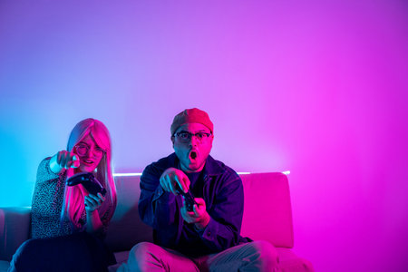 Young man and woman sitting on sofa with joy stick. Happy couple Professional Streamer holding...