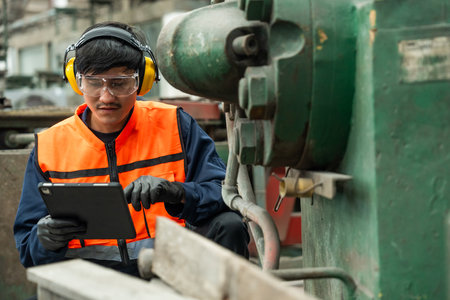 Confident engineer man with safety helmet standing analyzing with tablet in factory warehouse. Asian technician factory inspection and control machinery in industry factory.の写真素材