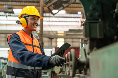Confident engineer man with safety helmet standing analyzing with tablet in factory warehouse. Asian...