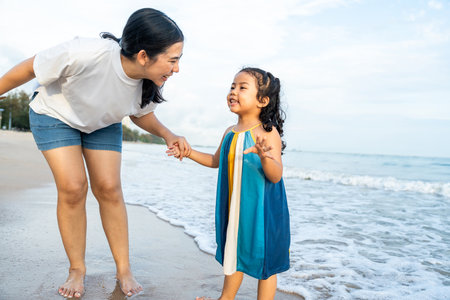Happy young asian mother and her child walking and holding hands on the beach and enjoy a sunset by...