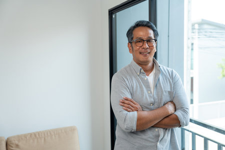 Handsome asian mature old man standing near windows with sunlight in the morning. Happy Portrait of cheerful smiling senior asian man pose looking at camera. Mature People and lifestyleの写真素材