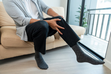 Close up old man leg knee pain feet. Mature senior man pain with ankle because walk too much. Massaging suffering knee foot. Pain at calves sitting on couch at home. Hands massage legs on sofa.の写真素材