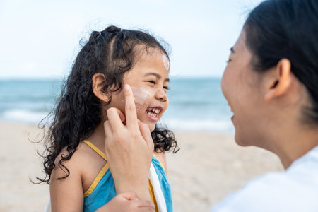 Asian mom applying sunscreen to her happy childâs face on the beach for skin protection from the sun. a young mother carefully smears protective cream on her daughterâs face for safe outdoor fun.の写真素材