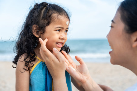Asian mom applying sunscreen to her happy childâs face on the beach for skin protection from the sun. a young mother carefully smears protective cream on her daughterâs face for safe outdoor fun.の写真素材
