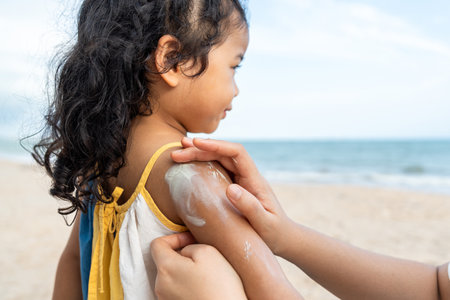 Asian mom applying sunscreen to her happy childâs face on the beach for skin protection from the sun. a young mother carefully smears protective cream on her daughterâs face for safe outdoor fun.の写真素材